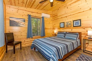 Een houten slaapkamer met een bed, een stoel, een raam met gordijnen en ingekaderde foto's aan de muur.
