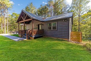 A log cabin with a porch, a covered deck, and a well-maintained lawn.