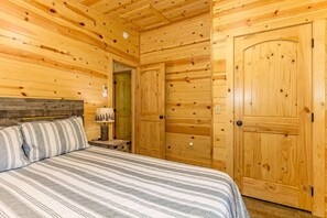 Een slaapkamer met houten lambrisering, een bed, een nachtkastje en een deur.