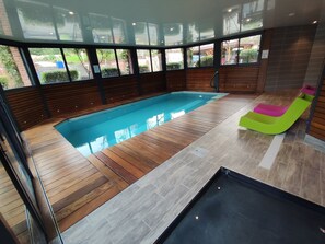 A modern indoor swimming pool with wooden flooring and a colorful slide.