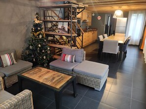 Una sala de estar acogedora con un árbol de Navidad, muebles de mimbre, una mesa de centro de madera y una cocina al fondo.