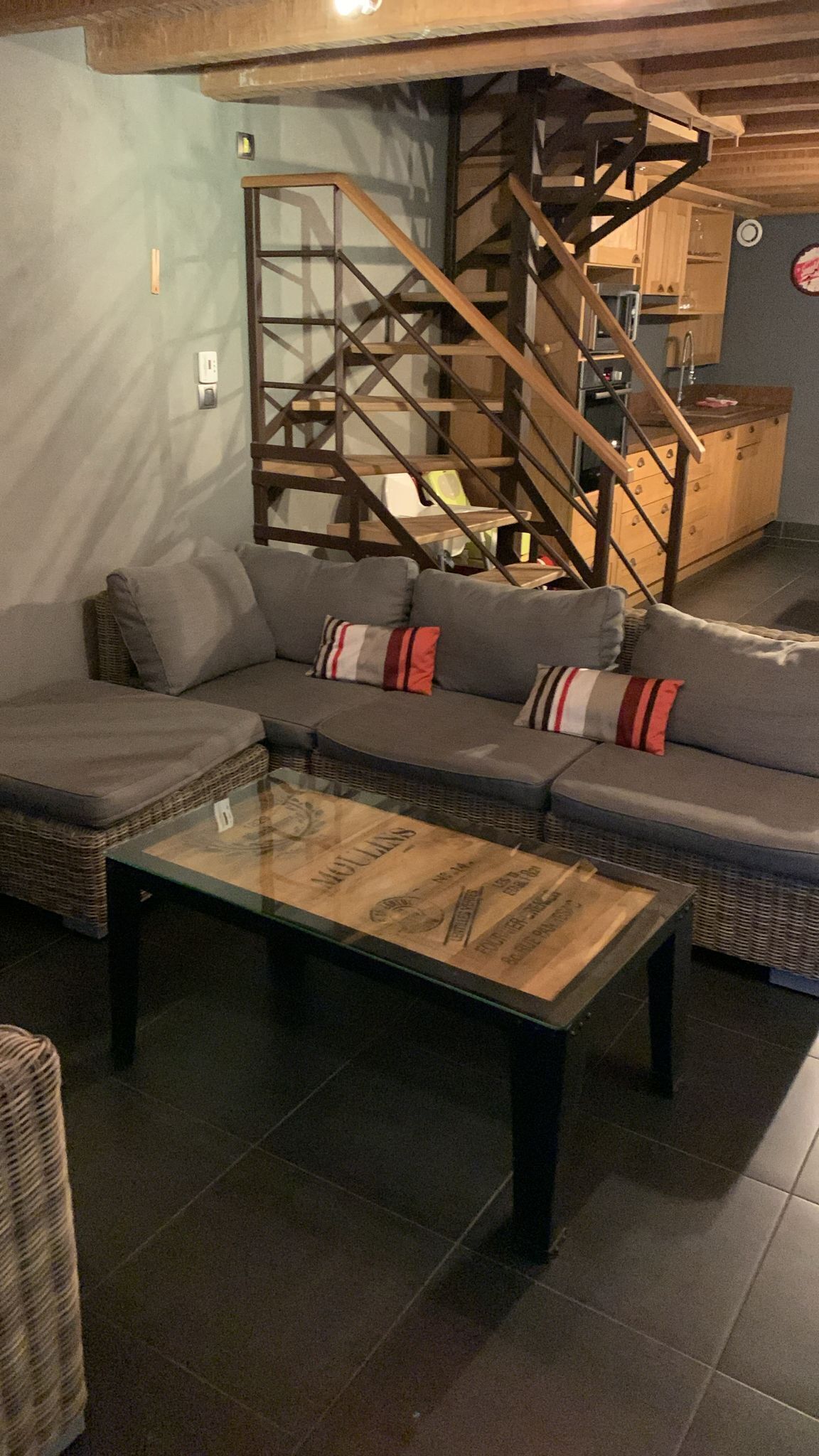 A living room with a sectional sofa, a glass coffee table, and a wooden staircase.