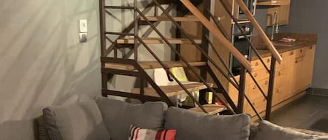 Una sala de estar con un sofá seccional, una mesa de centro de vidrio y una escalera de madera.