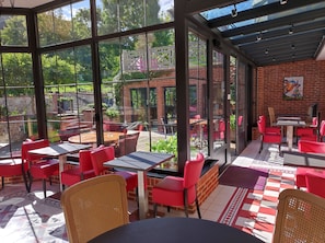 Un restaurante con amplios ventanales, sillas rojas y una pared de ladrillo.
