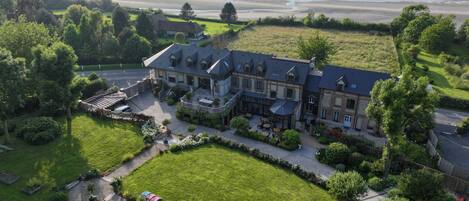 A large, multi-story building with a spacious courtyard, surrounded by lush greenery and a view of the sea.