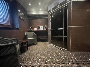 Ein modernes Badezimmer mit gefliestem Boden, einer Duschkabine aus Glas und einer Sitzecke mit Stühlen.