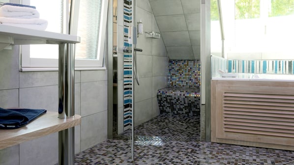 A bathroom with a tiled floor, a shower area, and a window.