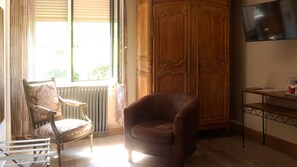 Una habitación con un armario de madera, un sillón de cuero marrón, una butaca tapizada de blanco, un radiador y un televisor sobre un mueble bajo.