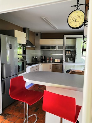 Une cuisine moderne avec des appareils en acier inoxydable, un tabouret de bar rouge et une horloge suspendue.