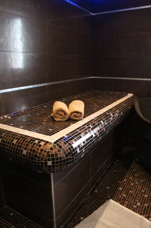 Ein Badezimmer mit gefliestem Boden, einer Bank mit Handtüchern und einem Stuhl.