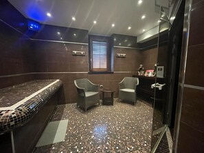 A modern bathroom with a bench, two chairs, a small table, and a shower area.