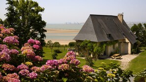 Une maison avec un toit en pente, une cheminée et une vue sur la plage et la mer.