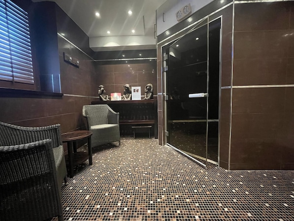 Une salle de bain moderne avec un sol carrelé, une douche en verre et un coin salon avec des chaises.