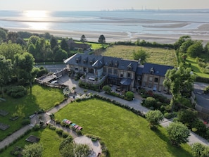 Un grand immeuble à étages, doté d’une cour spacieuse, entouré d’une végétation luxuriante et offrant une vue sur la mer.
