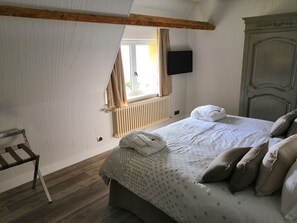 Makuuhuoneessa on puinen kattopalkki, kuviollinen peitto sängyllä, yöpöytä, patteri ja seinälle asennettu televisio.