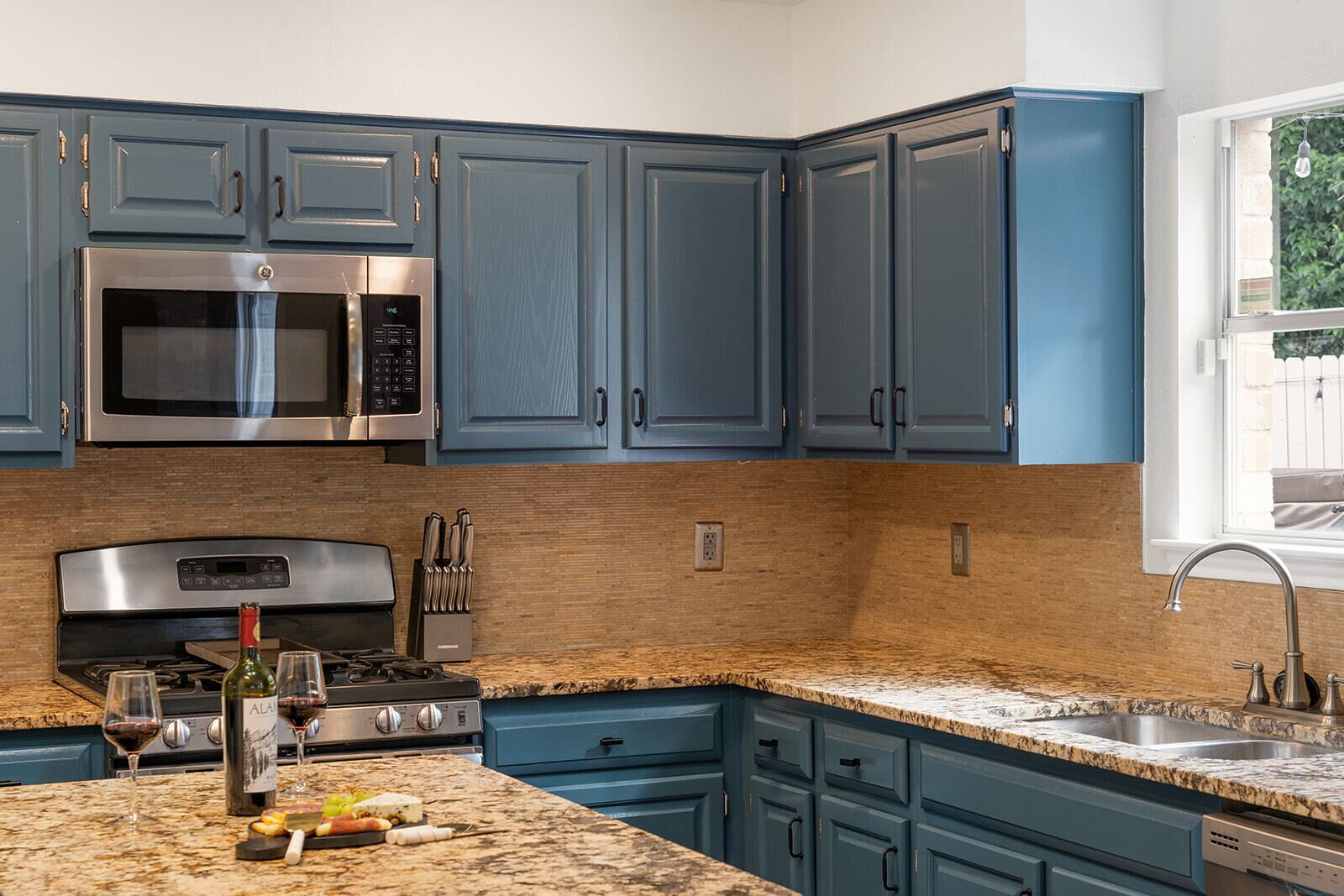 A modern kitchen with blue cabinets, stainless steel appliances, granite countertops, and a built-in dishwasher.