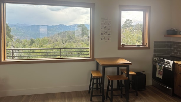 A kitchen with a large window offering a mountain view, a small table, two stools, and a tiled backsplash. - Cozy studio in charming Ridgway, CO (Ridgway)
