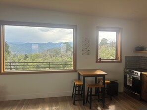 A kitchen with a large window offering a mountain view, a small table, two stools, and a tiled backsplash. - Cozy studio in charming Ridgway, CO (Ridgway)