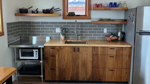 A modern kitchen with a microwave, oven, and stainless steel appliances. There are wooden cabinets and a window above the sink. - Cozy studio in charming Ridgway, CO (Ridgway)
