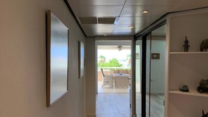 A hallway with a wooden floor, framed pictures on the wall, and a sliding glass door leading to an outdoor area with wicker furniture. - Curacao,Piscadera Bay, next to Marriott, Very luxuriously furnished Apartment (Willemstad)