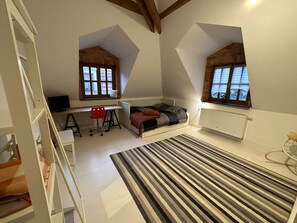 Una habitación pequeña con cama, escritorio y dos ventanas.