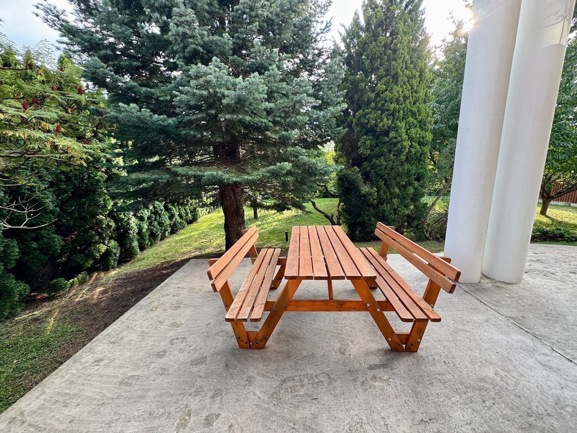 A picnic table with benches in a park with trees and a concrete path.