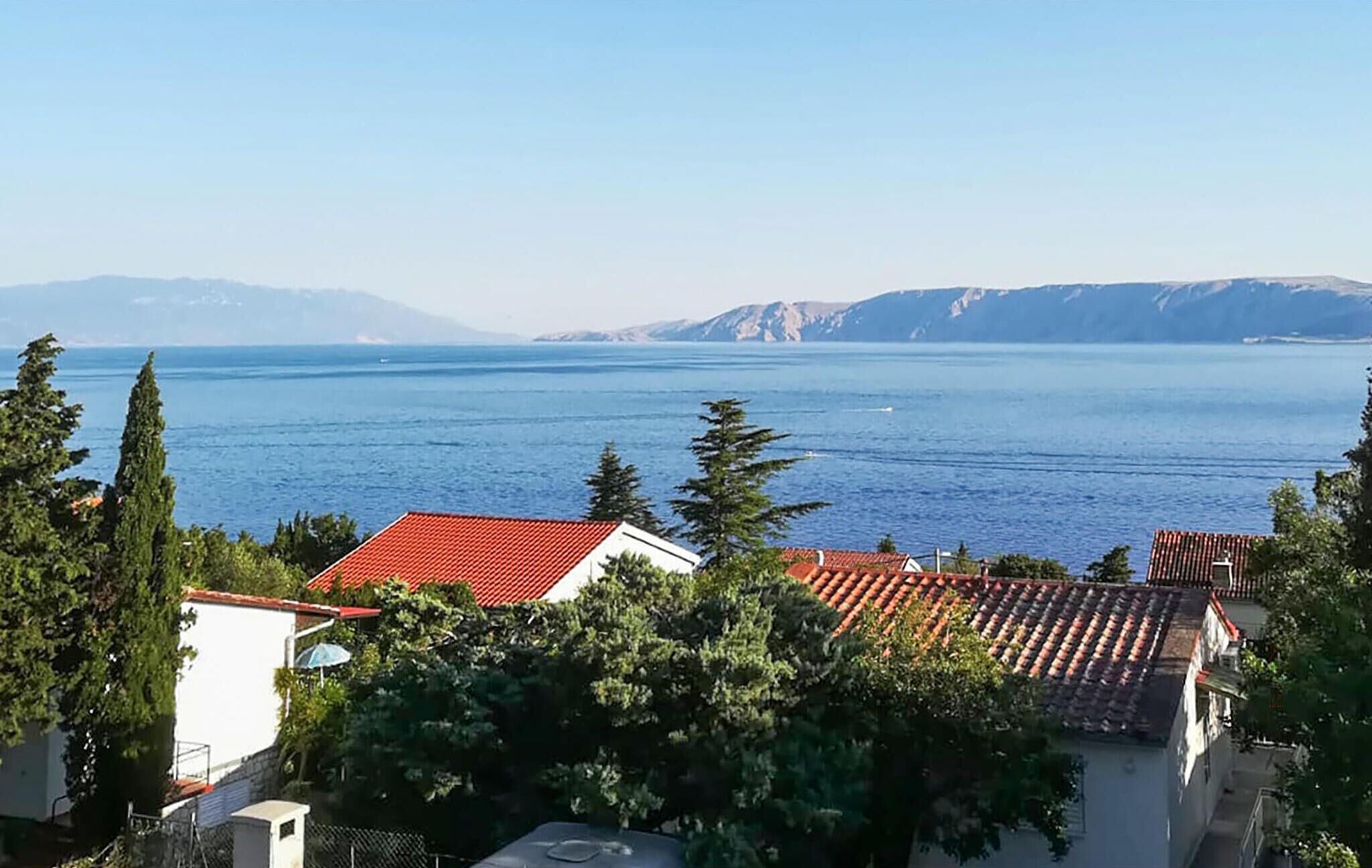 A coastal view with buildings, trees, and a clear blue sea.
