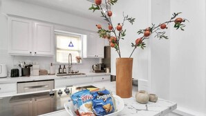 A modern kitchen with white cabinets, a marble countertop, and a decorative pomegranate tree in a vase. - *Pool | Near Galleria Mall, NRG stadium (Houston)