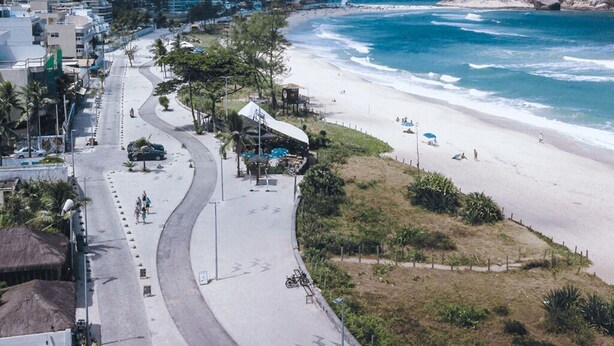 A coastal road with a beach on one side and buildings on the other. - Apartamento e Deck com vista mar - Loft Rocha (Rio de Janeiro)