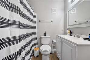 Un baño con cortina de ducha a rayas, un inodoro, un lavabo con espejo y un secador de manos.
