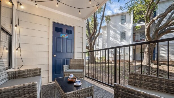 A covered outdoor seating area with wicker furniture and a table, a blue door, and a view of neighboring houses. - THE LITTLE HAVANA AT RIVERSIDE #11 (Austin)