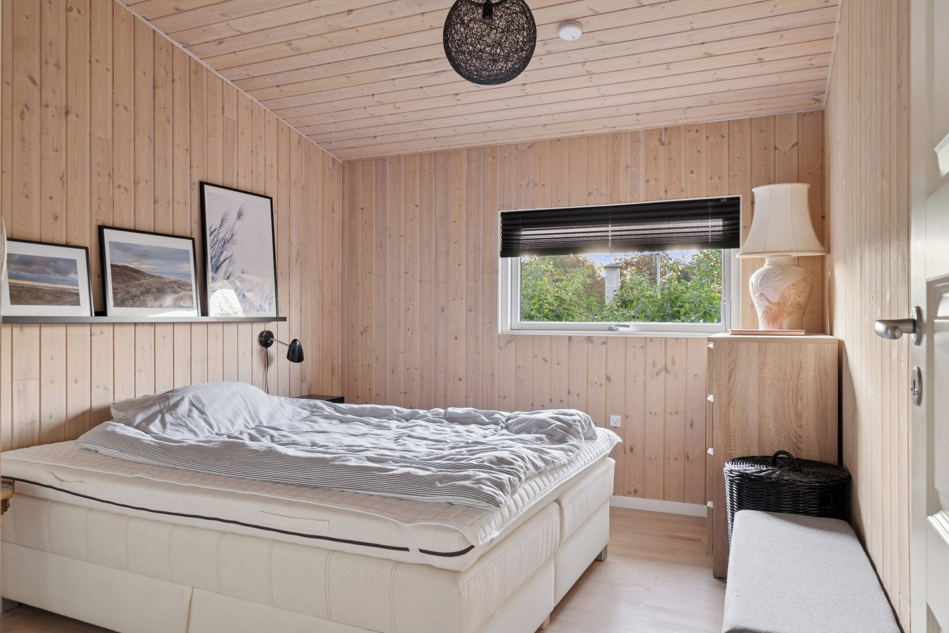 A bedroom with a bed, a window with blinds, a lamp, and framed pictures on the wall.