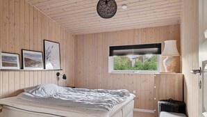 A bedroom with a bed, a window with blinds, a lamp, and framed pictures on the wall. - Active coastal holiday in cozy cottage (Slagelse)