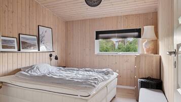 A bedroom with a bed, a window with blinds, a lamp, and framed pictures on the wall.