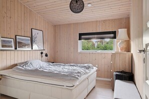 A bedroom with a bed, a window with blinds, a lamp, and framed pictures on the wall. - Active coastal holiday in cozy cottage (Slagelse)
