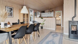 A modern interior with a wooden dining table, black chairs, a large pendant light, a fireplace, and a kitchen area. - Active coastal holiday in cozy cottage (Slagelse)