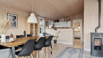 A modern interior with a wooden dining table, black chairs, a large pendant light, a fireplace, and a kitchen area.