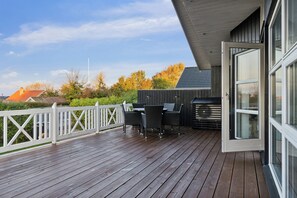 An outdoor deck with a table and chairs, a white fence, and a building with large windows.