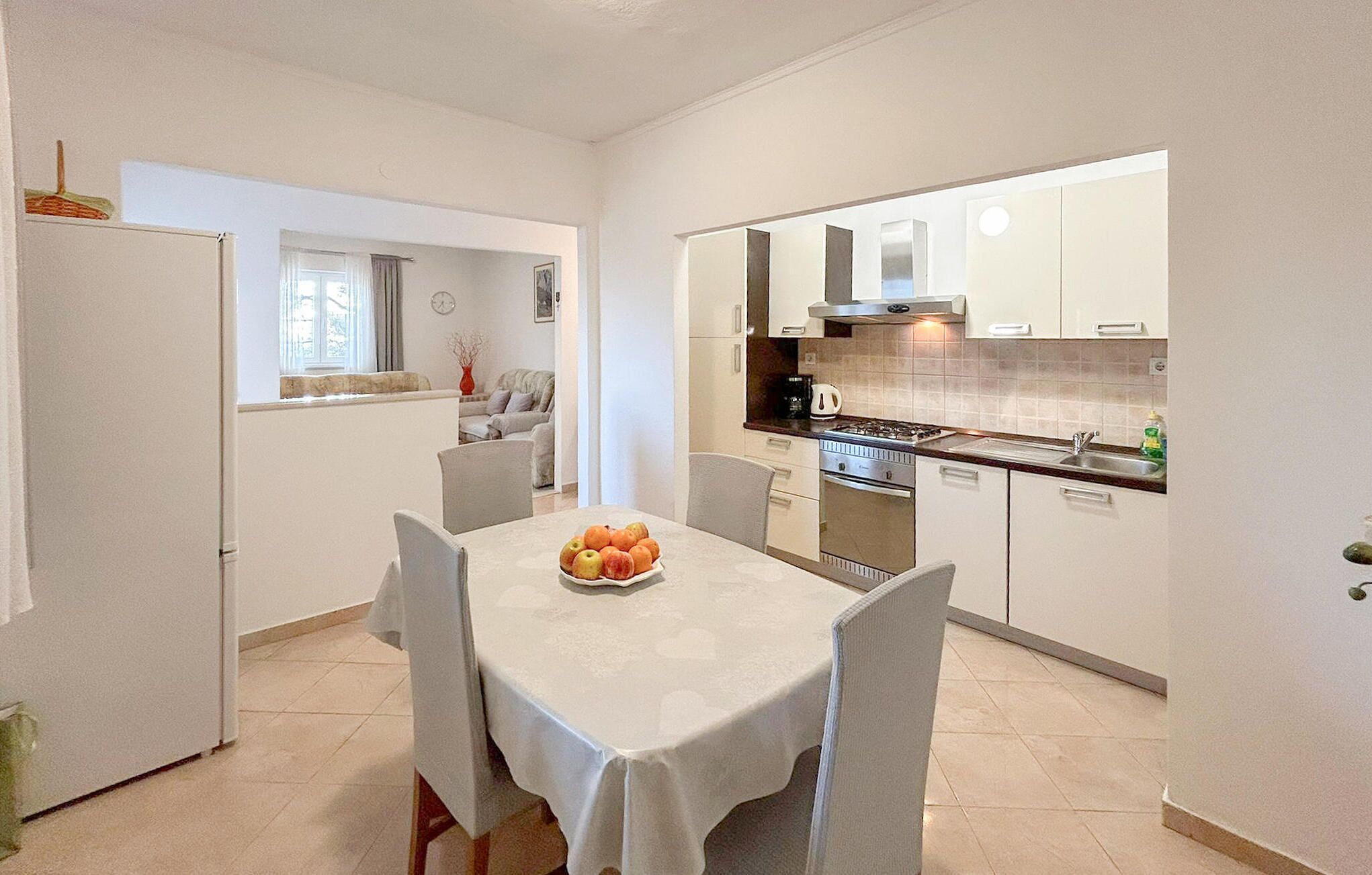 A compact kitchen with white cabinets, a dining table with chairs, and a fruit bowl on the table.