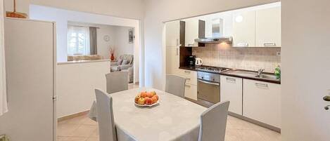 A compact kitchen with white cabinets, a dining table with chairs, and a fruit bowl on the table.
