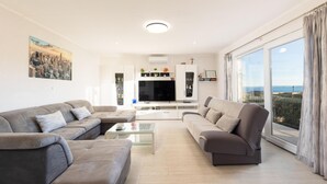 A modern living room with two sofas, a coffee table, and a TV. There is a large window with a view of the landscape.