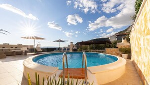 A rooftop pool with a clear view of the sea, surrounded by lounge chairs and umbrellas.