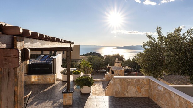 A rooftop terrace with a stone wall, a pergola, and a view of the sea.