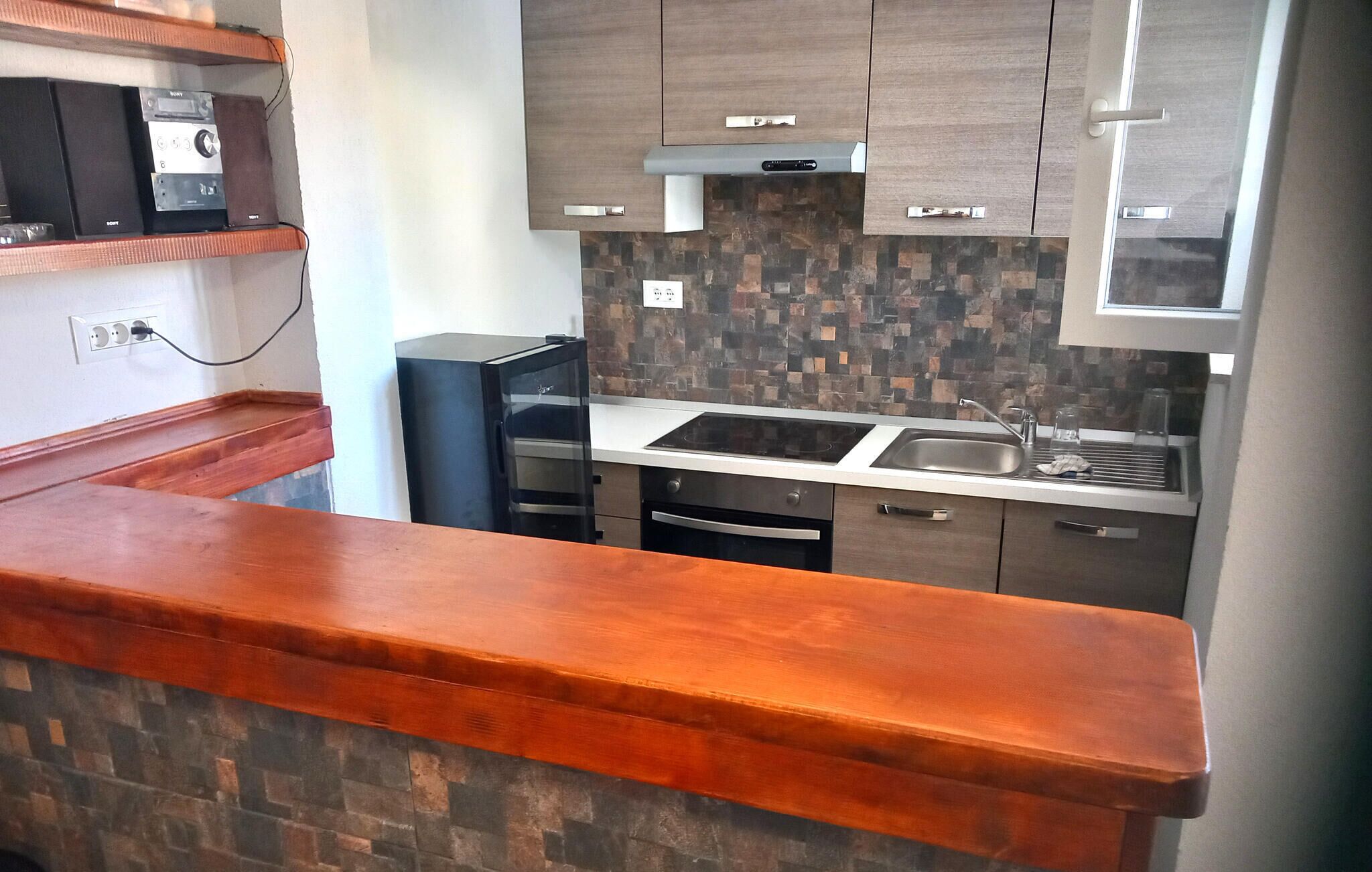 A modern kitchen with a built-in oven, a stainless steel sink, and wooden cabinets.