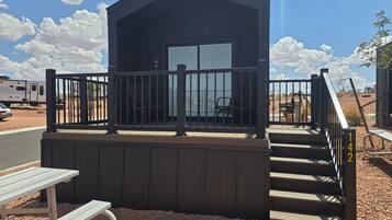A small wooden cabin with a balcony, a bench, and a staircase leading to the entrance.