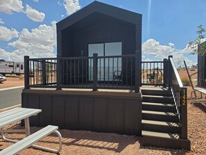 A small wooden cabin with a balcony, a bench, and a staircase leading to the entrance.