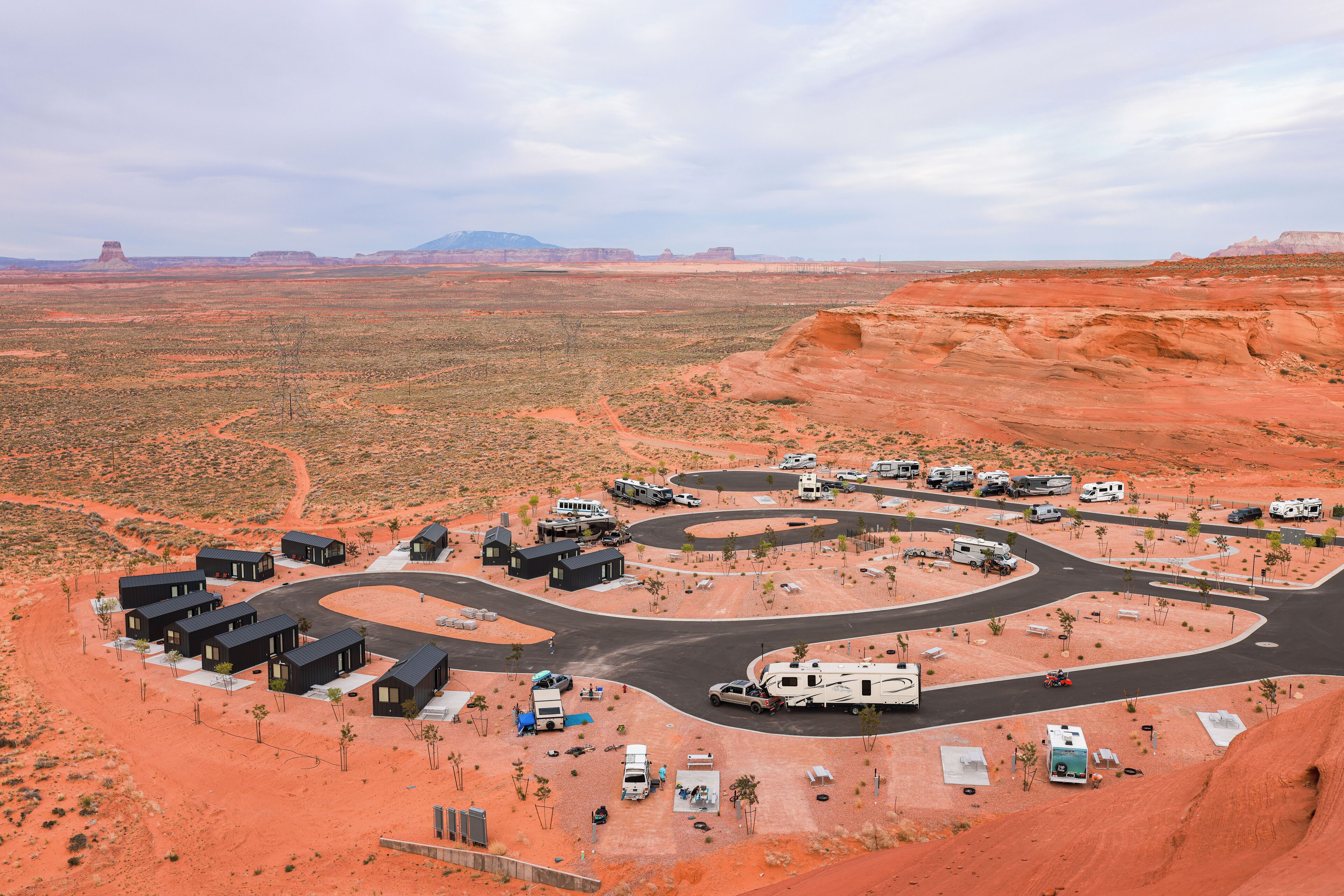 Paisaje desértico con un camping que incluye vehículos recreativos, tiendas de campaña y casas móviles.
