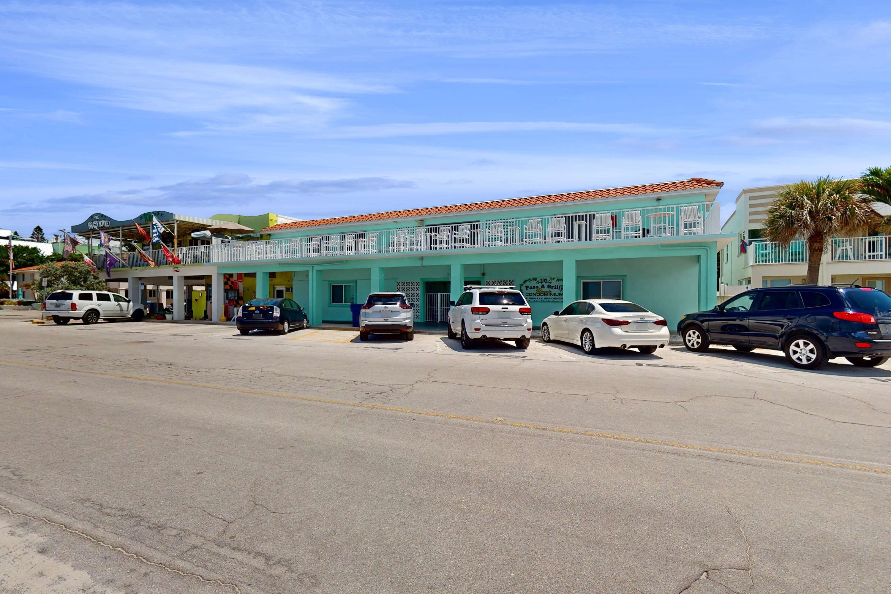 A building with a light blue facade, multiple balconies, and a parking lot with several cars.