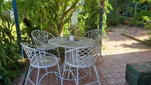 A white metal outdoor table and chairs set on a brick patio surrounded by lush greenery. - Magnolia Cottage- wineries, main street, station (Croydon North)