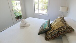 A hotel room with a large bed, two decorative pillows, a rolled towel, and a window with a view of greenery. - Magnolia Cottage- wineries, main street, station (Croydon North)